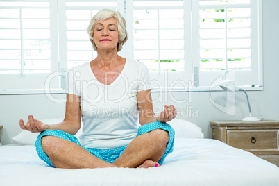 Senior woman doing yoga on bed