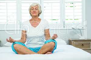 Senior woman doing yoga on bed