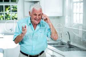 Senior man talking on phone in kitchen