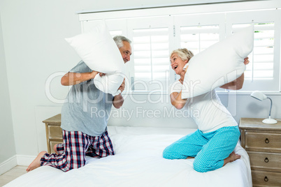Senior couple playing with pillows on bed