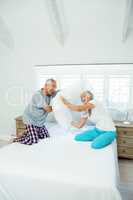 Old couple playing with pillows on bed