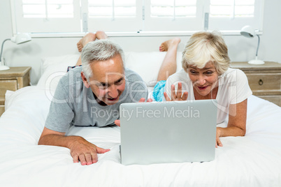 Senior man and woman using laptop on bed at home