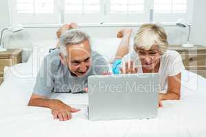 Senior man and woman using laptop on bed at home