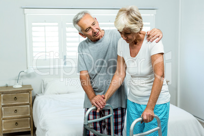 Senior woman with walker by man in bedroom