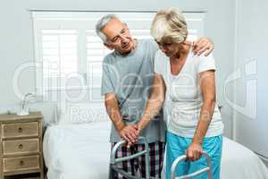 Senior woman with walker by man in bedroom