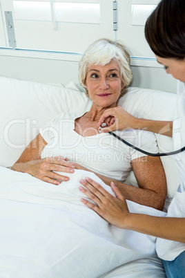 Female doctor auscultating old woman with stethoscope