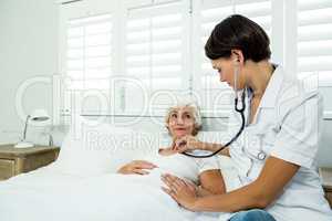 Female doctor auscultating aged woman at home