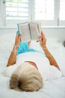 Rear view of senior woman holding book on bed