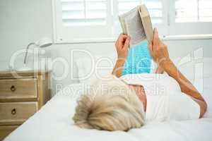 Rear view of old woman holding book on bed