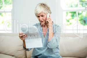 Senior woman reading document while talking on phone