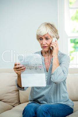 Aged woman reading document while talking on phone