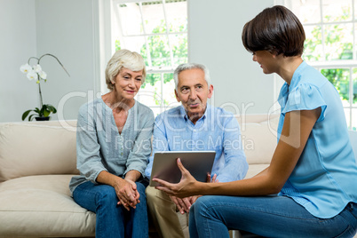 Female consultant showing digital tablet to aged couple at home