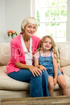 Portrait of smiling granny and girl sitting on sofa