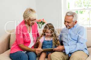 Happy grandparents and girl using digital tablet