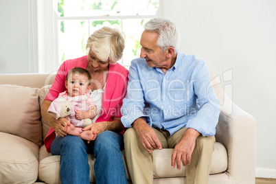 Happy grandparents looking at baby while siting on sofa