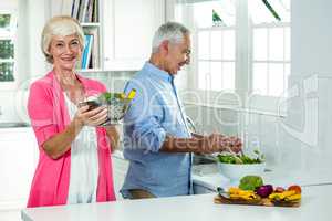 Smiling senior woman holding colander with man preparing vegetab
