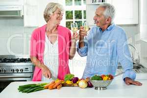Smiling senior couple toasting white wine while preparing vegeta