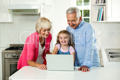 Grandparents and girl using laptop in kitchen