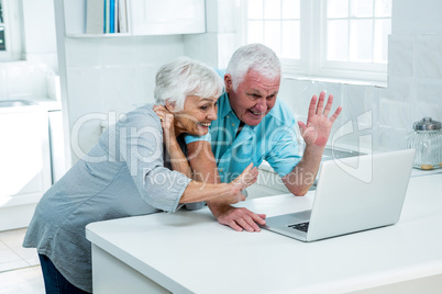 Happy senior couple gesturing while using laptop