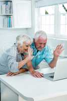 Senior couple waving hands while using laptop