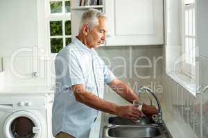 Calm senior man filling water in glass while standing at sink