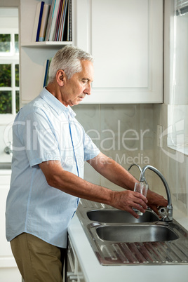 Senior man filling water in glass while standing at sink