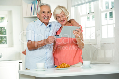 Happy senior couple with credit card while using digital tablet