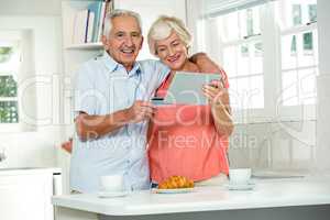 Happy senior couple with credit card while using digital tablet