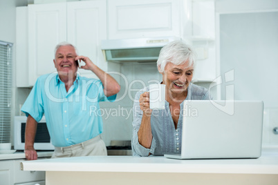 Happy woman using laptop while senior man talking on phone