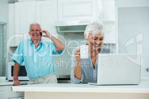 Happy woman using laptop while senior man talking on phone