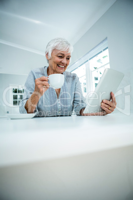 Happy retired woman having coffee while using tablet