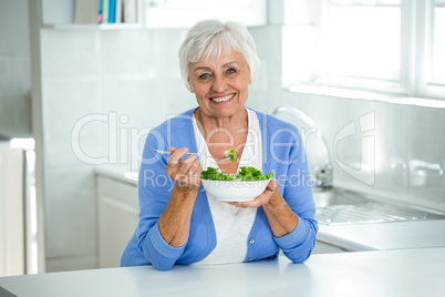 Happy senior woman with salad in kitchen