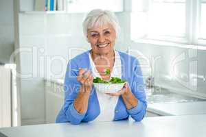 Happy senior woman with salad in kitchen