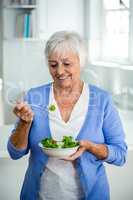 Senior woman eating salad while standing in kitchen
