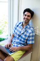 Portrait of man sitting on bed and using laptop
