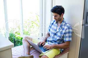 Young man sitting on bed and using laptop