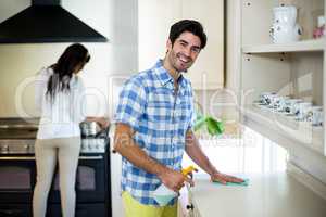 Man cleaning the kitchen and woman cooking food in background