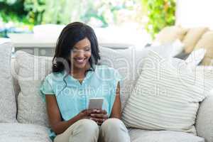 Young woman sitting on sofa and text messaging on phone