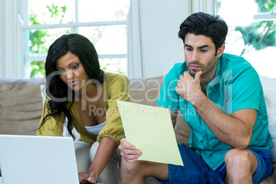 Thoughtful man checking at bills while woman using laptop