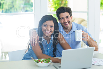 Portrait of young couple using laptop while having breakfast