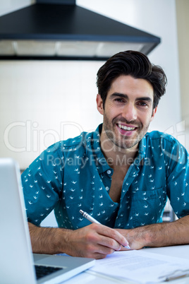 Portrait of man writing on clipboard in kitchen