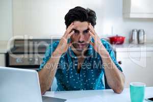 Tensed man sitting with bills and laptop in kitchen