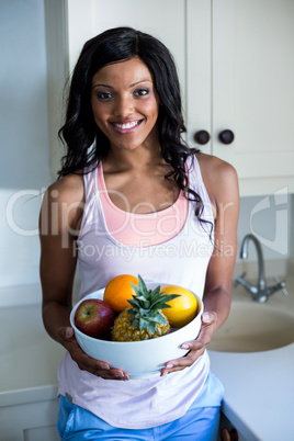 Portrait of young woman standing with bowl of fruits