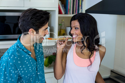 Woman feeding man while cooking in kitchen