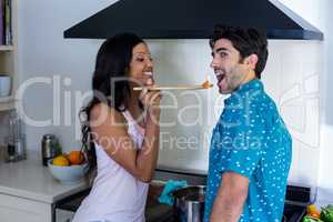Woman feeding man while cooking in kitchen
