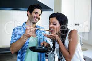Man feeding woman while cooking in kitchen