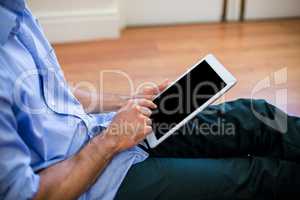 Mid-section of man sitting on floor and using digital tablet