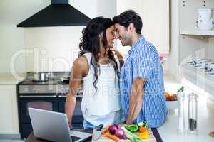 Young couple embracing while using laptop in kitchen