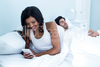 Woman checking her mobile phone while man sleeping on bed