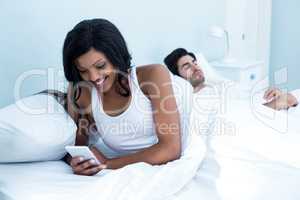 Woman checking her mobile phone while man sleeping on bed